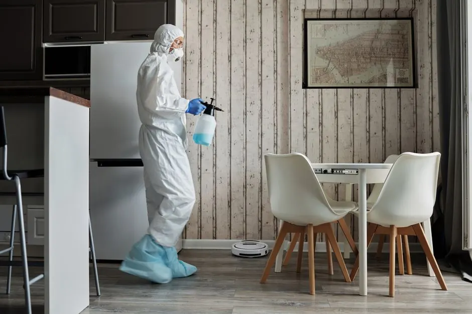 Person in protective suit using disinfectant in a contemporary living area during the COVID-19 pandemic.